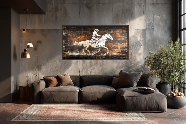 Rustic cowboy on a white horse canvas wall art displayed above a dark sofa in a modern room.