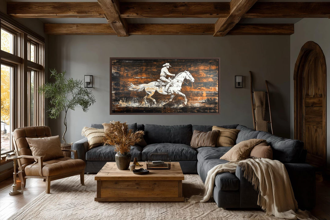 Rustic cowboy on horse wall art on dark wood planks in a cozy, modern farmhouse living room.