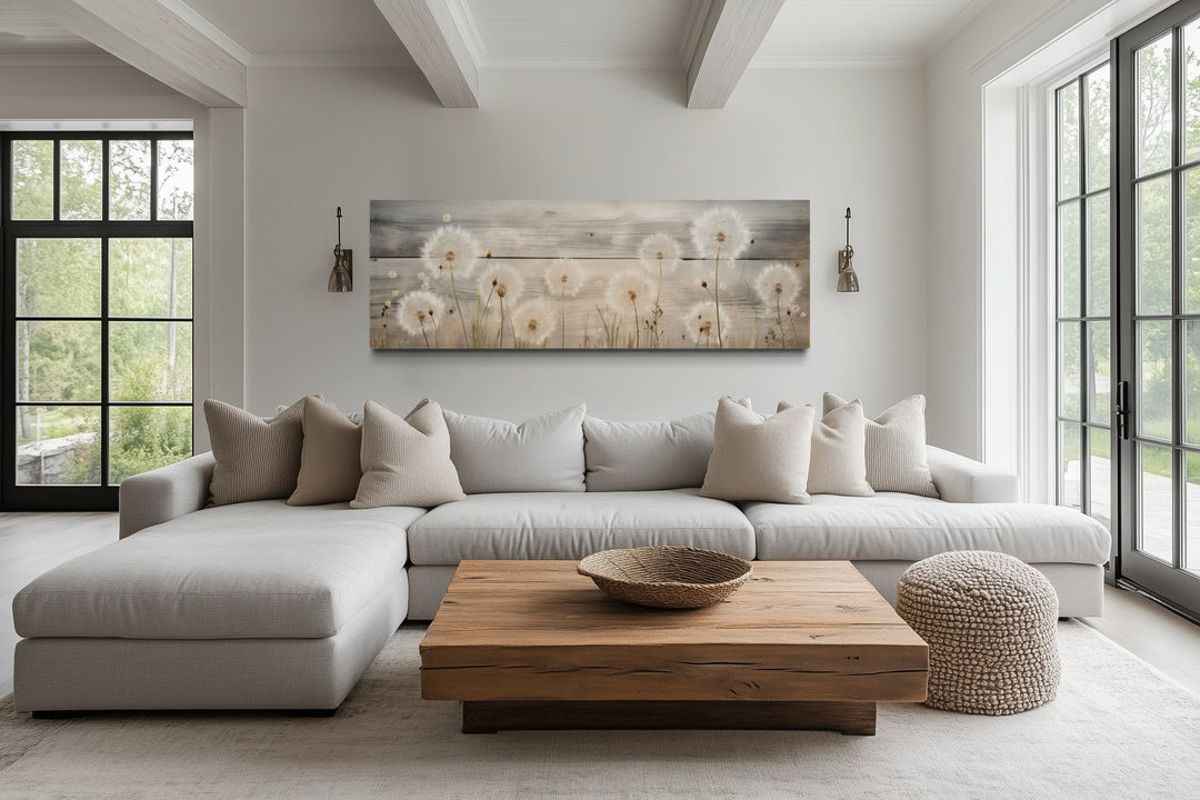 Rustic dandelion painting on wood, long horizontal wall art above a neutral sectional sofa.