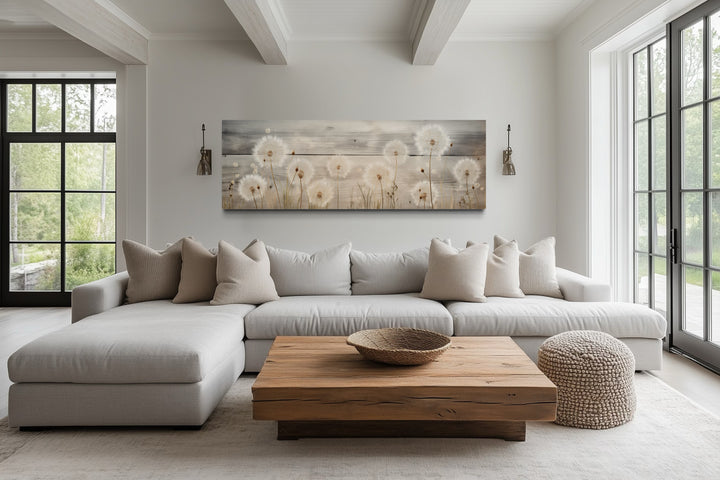 Rustic dandelion painting on wood, long horizontal wall art above a neutral sectional sofa.