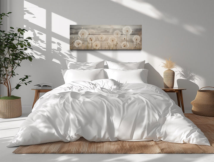 Rustic horizontal dandelion painting on wood texture hanging above a bed with white linens.
