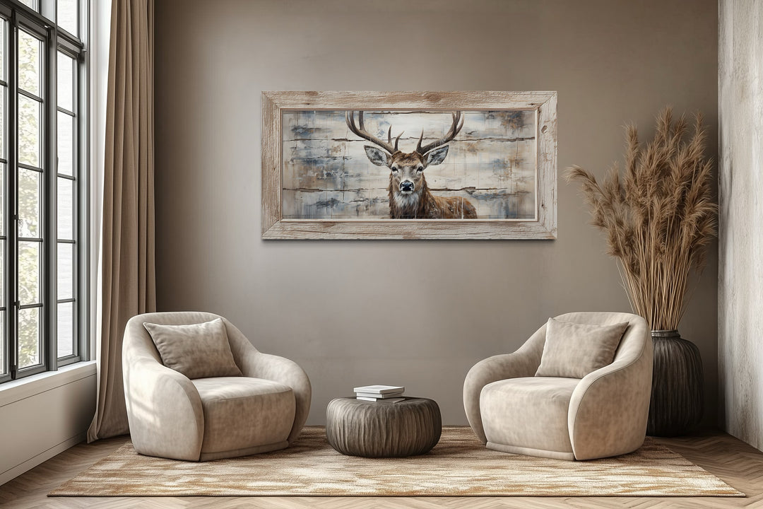 Rustic deer painting on wood canvas wall art in a wooden frame above two beige armchairs.
