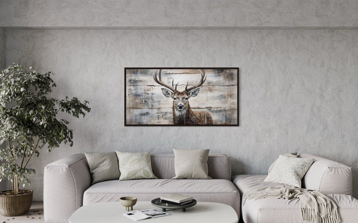 Rustic deer painting on wood canvas wall art in a dark frame above a modern beige sectional sofa.