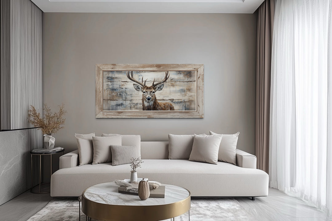Rustic deer painting on wood-look canvas in a wooden frame above a modern beige sofa.