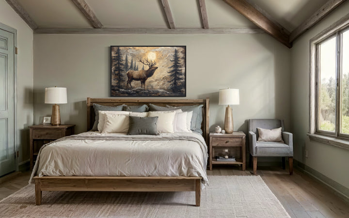 Rustic framed canvas wall art of an elk in a winter forest hanging above a bed in a cabin bedroom.
