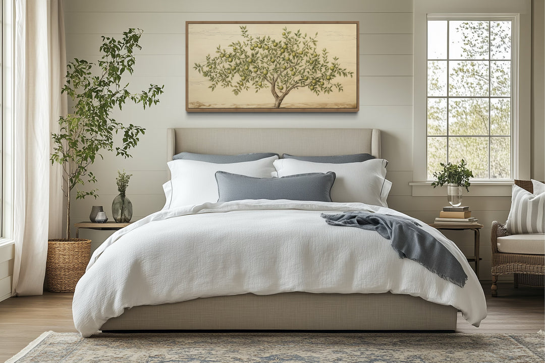 Rustic farmhouse apple tree canvas wall art in a wooden frame hanging above a cozy bed.