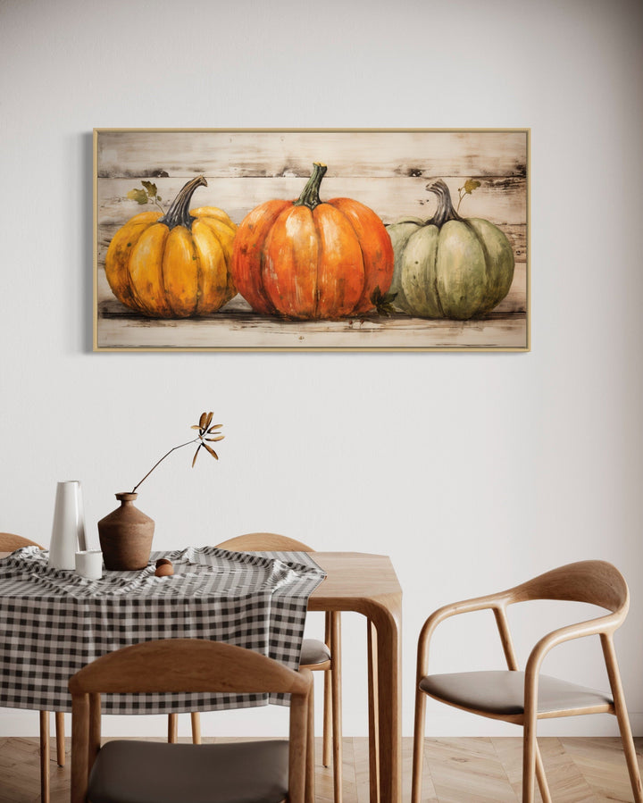 Framed canvas wall art of three pumpkins in orange, green, and yellow on a rustic wood background.