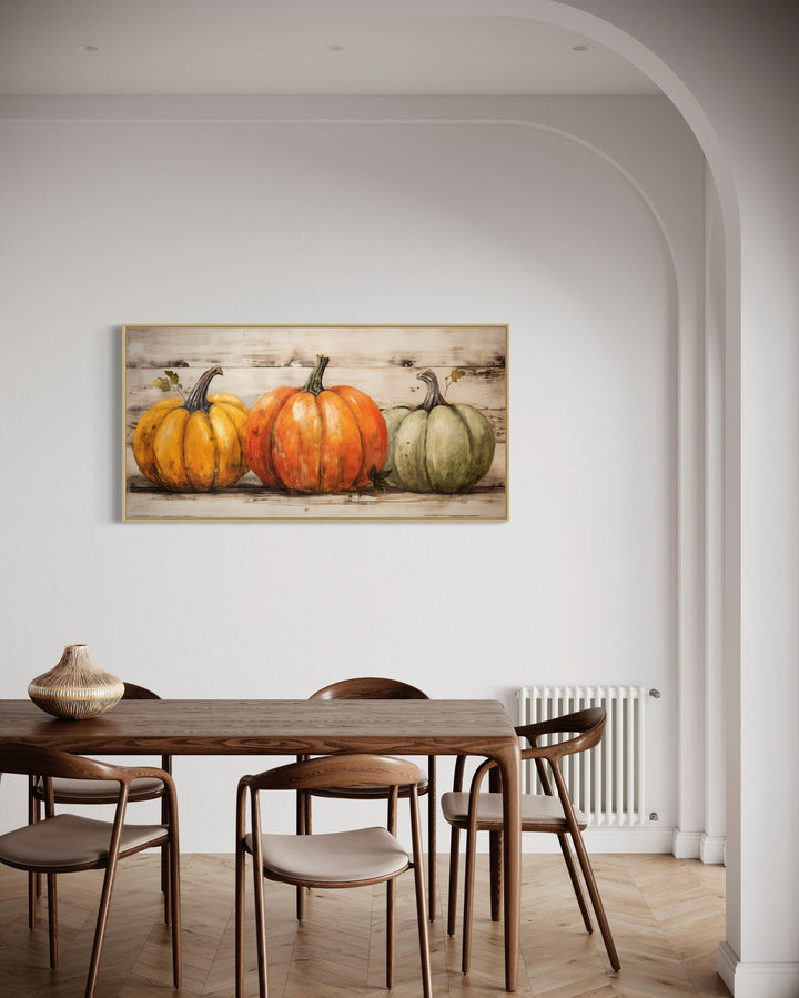 Rustic farmhouse wall art featuring three pumpkins on a wood-style background in a dining room.