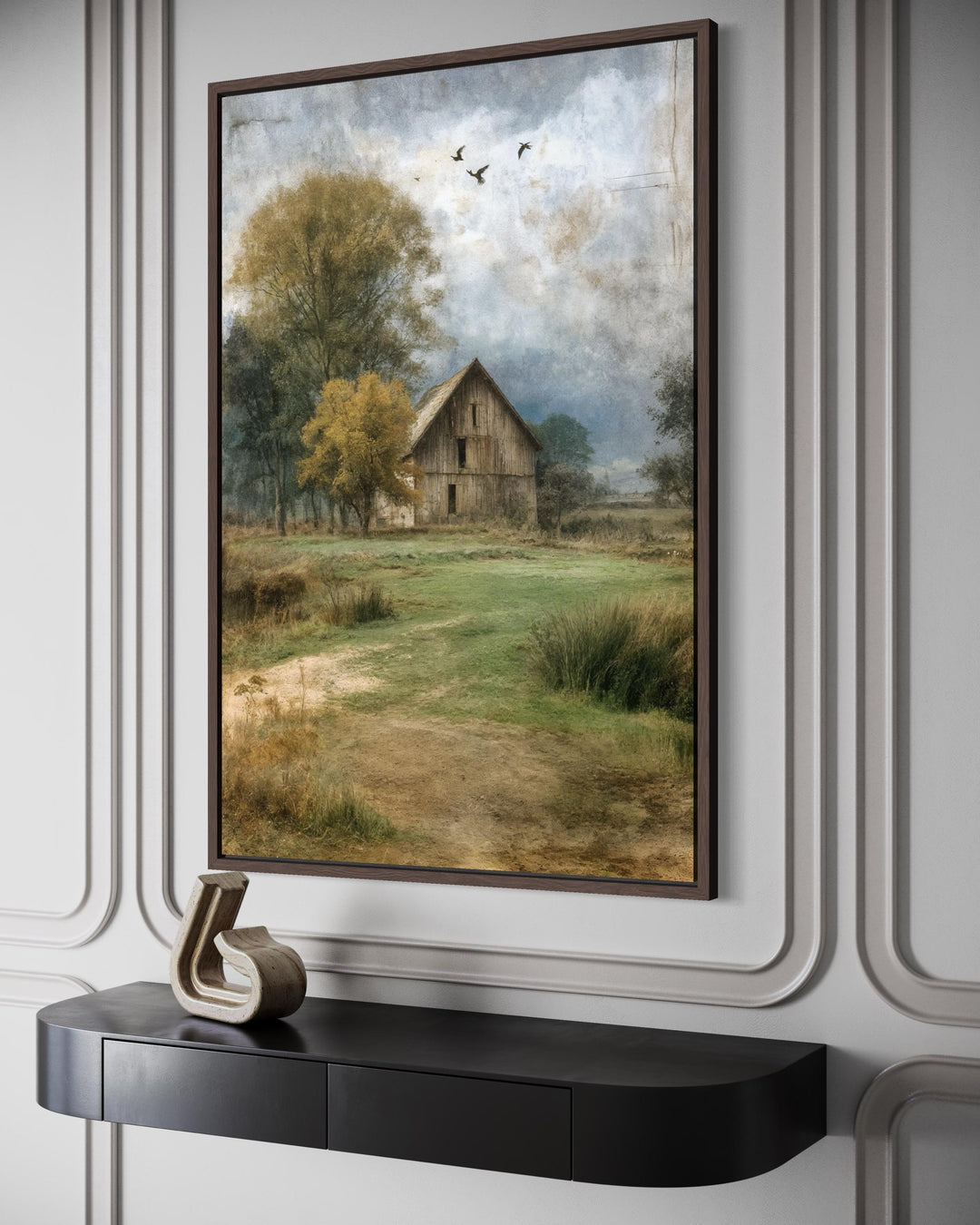 Vertical barn canvas print in a dark wood frame hanging above a modern black console table.