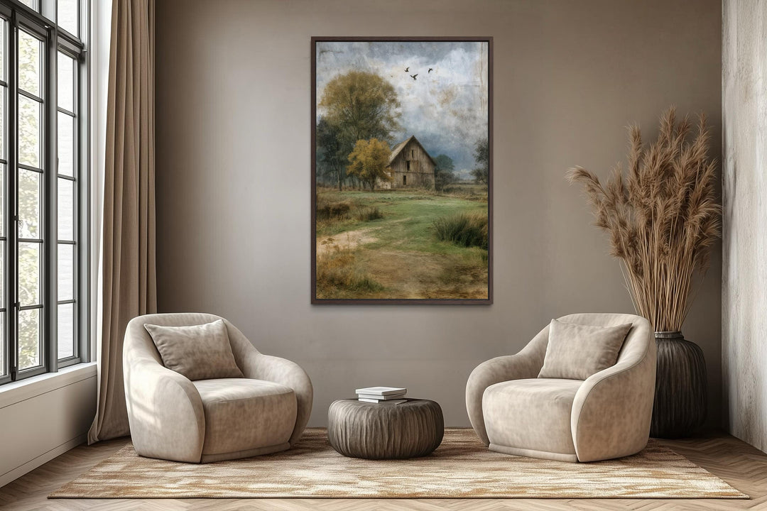 Vertical barn canvas print in a rustic farmhouse style hanging above two neutral armchairs.