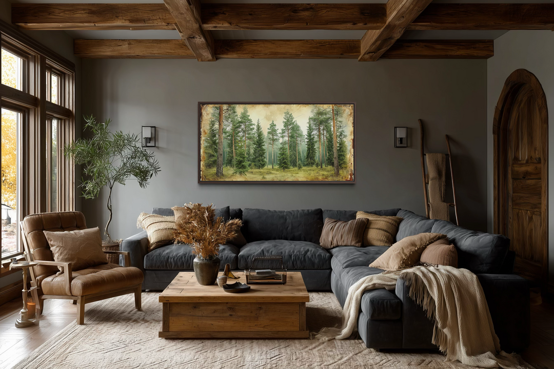 A wide framed canvas print of a rustic fir tree forest hangs in a cozy, wood-beamed living room.