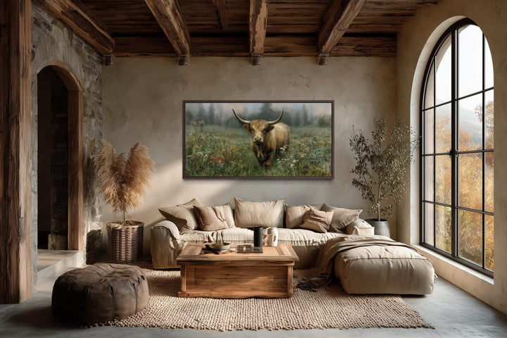 A rustic Highland cow canvas print hangs in a warm, earthy living room with exposed wooden beams.