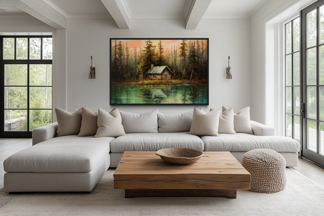 Rustic lake and cabin framed canvas wall art hanging above a modern sofa in a bright living room.