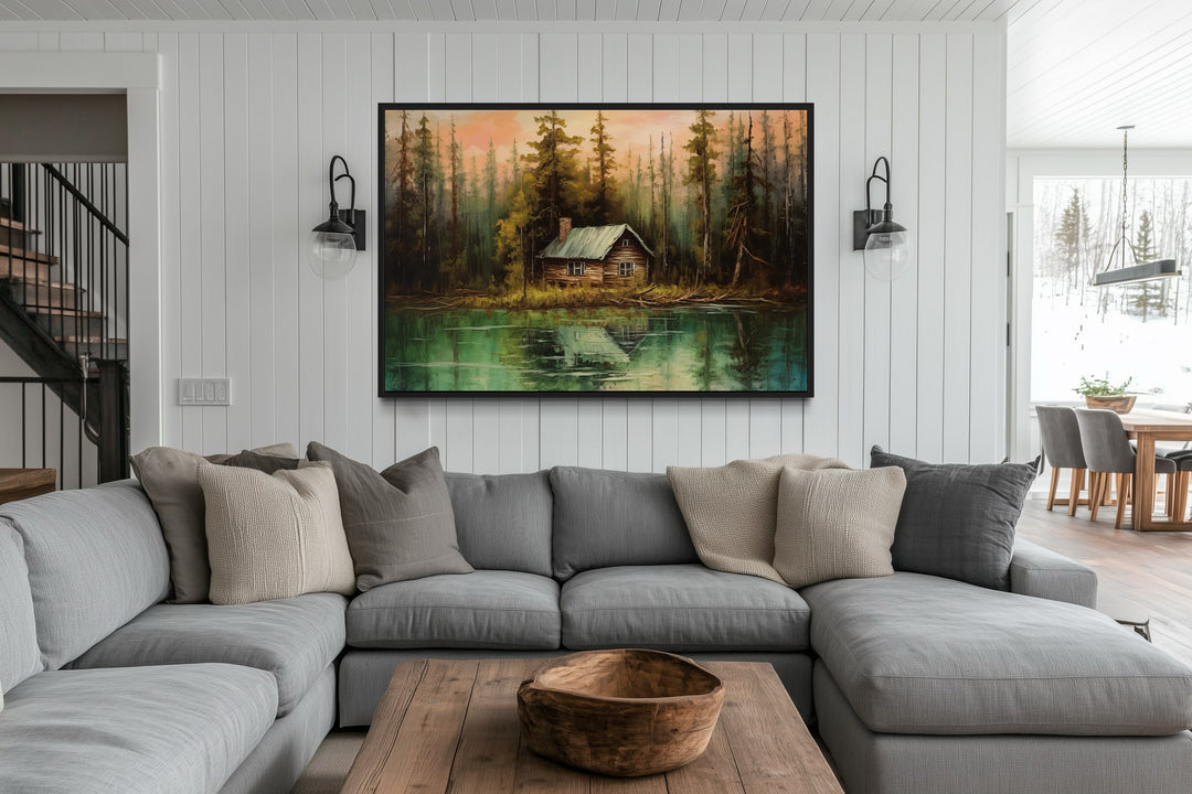 Rustic lake and cabin framed canvas wall art hanging above a grey sectional sofa in a living room.