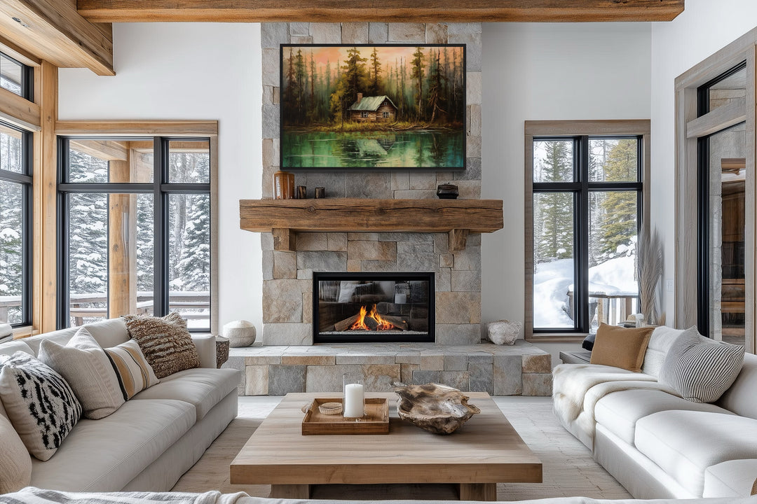 Rustic lake and cabin framed canvas wall art hanging above a stone fireplace in a cozy living room.