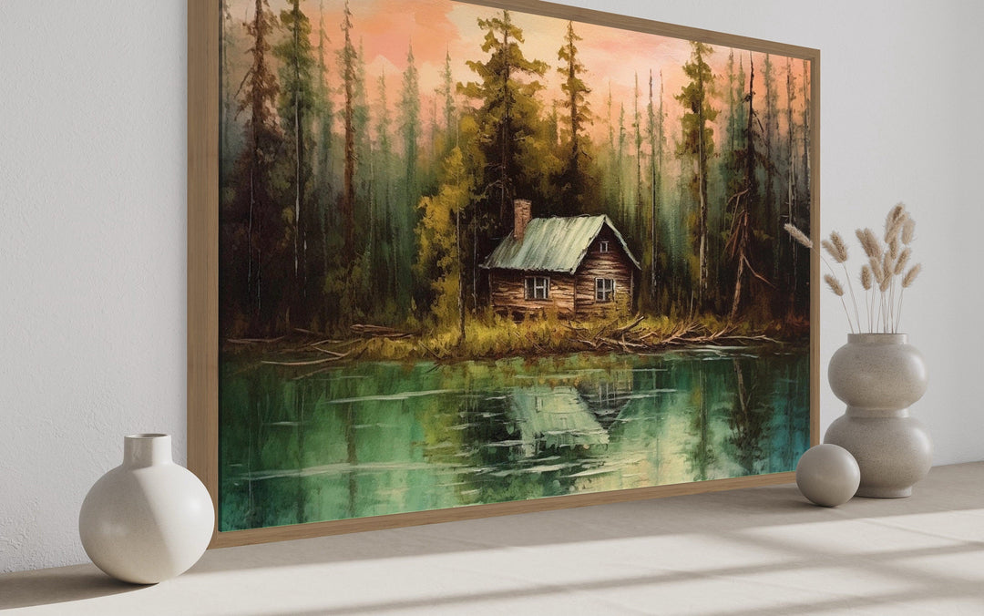 Rustic framed canvas wall art of a cozy cabin by a lake, surrounded by tall pine trees.