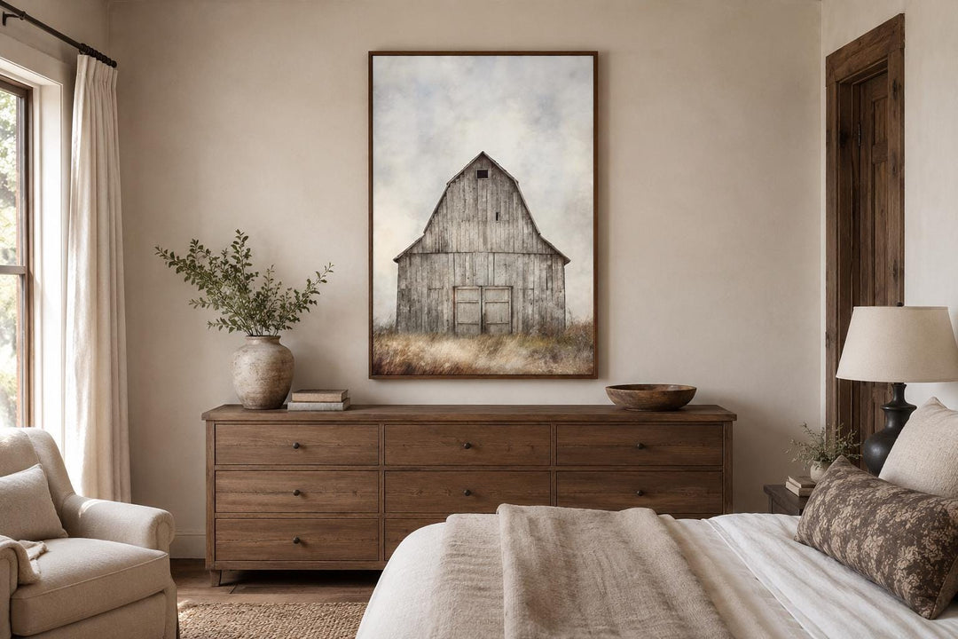 Vertical canvas print of a rustic weathered barn in a field above a wooden dresser in a bedroom.