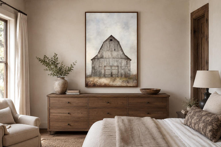 Vertical canvas print of a rustic weathered barn in a field above a wooden dresser in a bedroom.