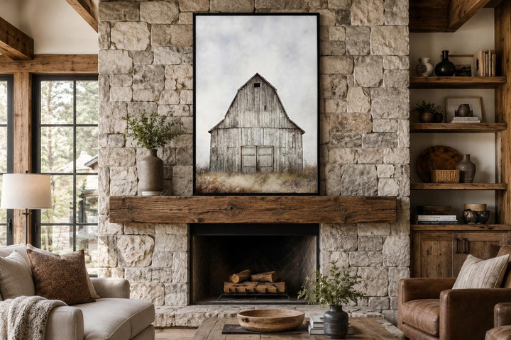 Vertical canvas print of a weathered rustic barn above a stone fireplace in a farmhouse living room.