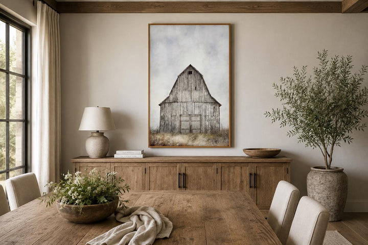 Vertical canvas print of a weathered rustic barn in a field above a wooden sideboard.
