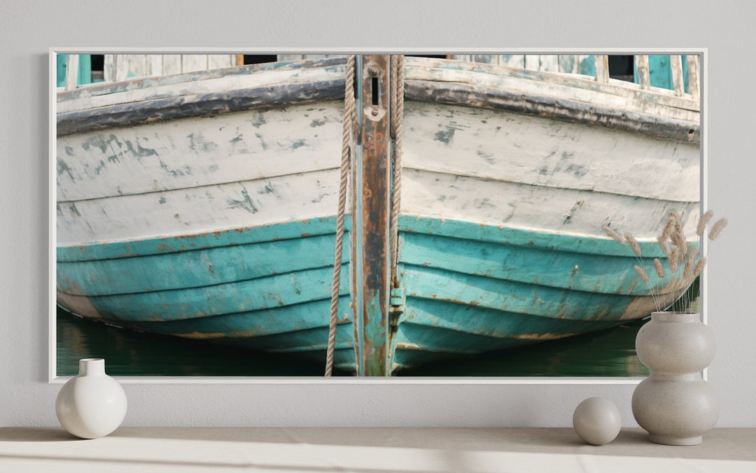 Framed canvas wall art of a rustic teal and white boat close-up on a wall with decorative vases.