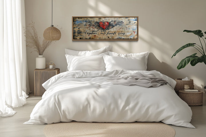 Rustic framed wall art with a winged heart and 'Together Our Hearts Sing' text above a white bed.