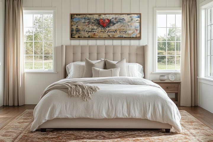 Rustic framed wall art over a bed featuring a winged heart and 'Together our hearts sing' text.