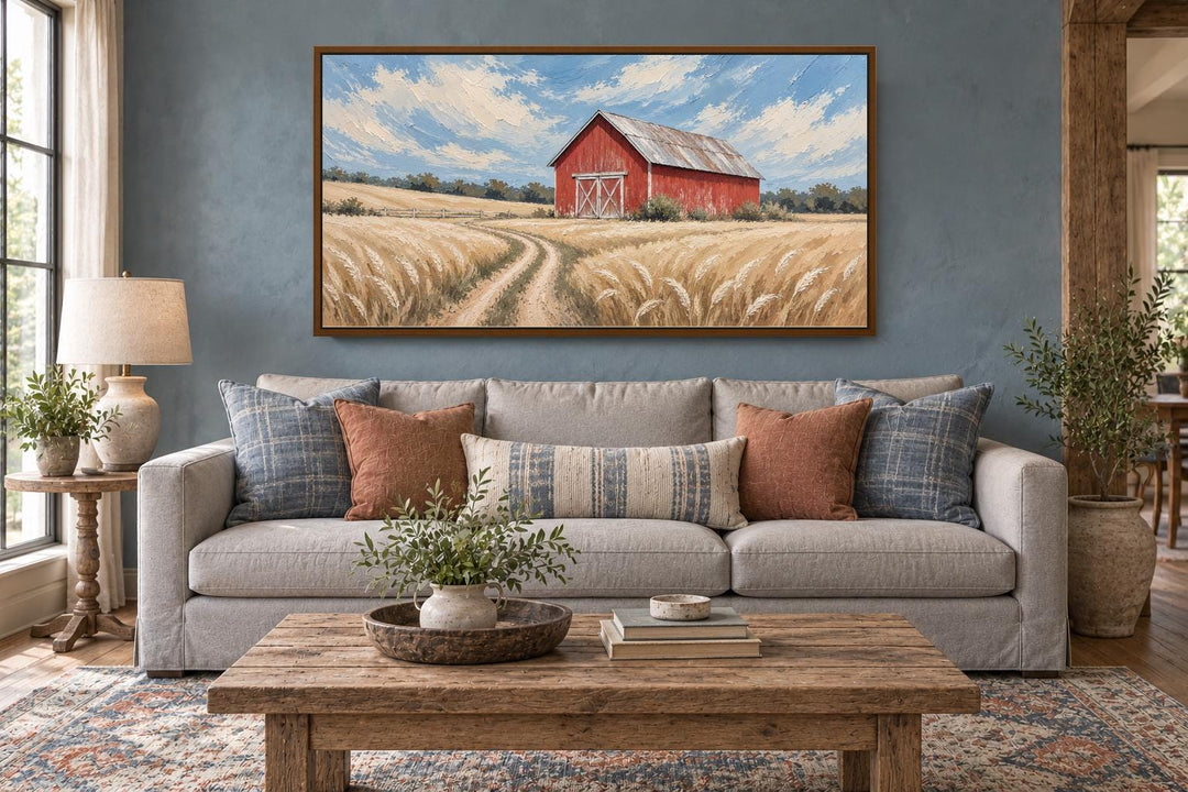 Rustic red barn in a golden wheat field landscape canvas wall art hanging above a neutral sofa.