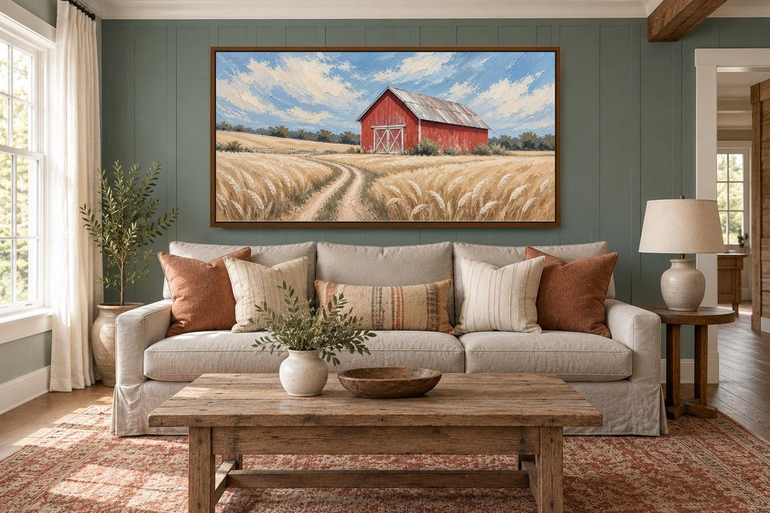 Rustic red barn in a golden wheat field landscape canvas wall art hanging above a neutral sofa.