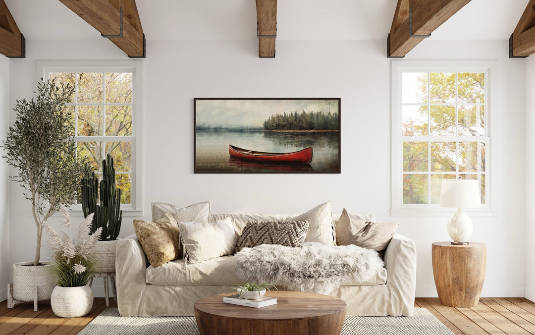 Rustic red canoe in the lake framed canvas wall art hanging above a sofa in a cozy living room.