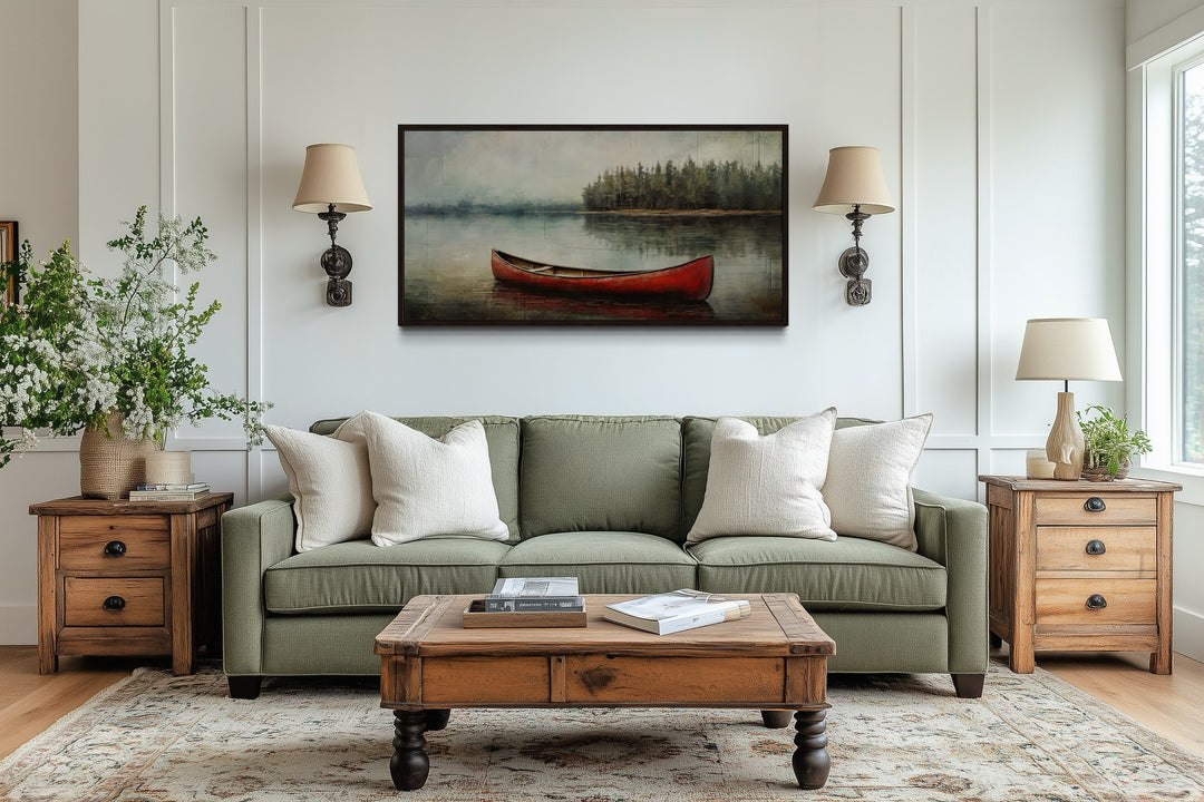 Rustic red canoe in a calm lake framed canvas wall art hanging above a green sofa in a living room.