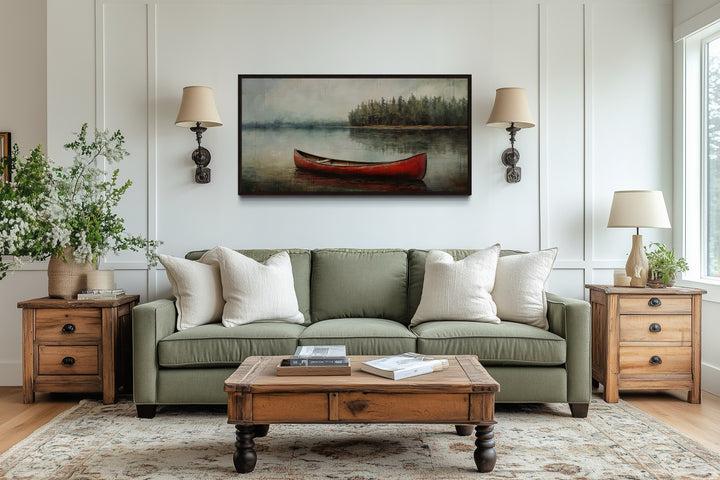 Rustic red canoe in a calm lake framed canvas wall art hanging above a green sofa in a living room.