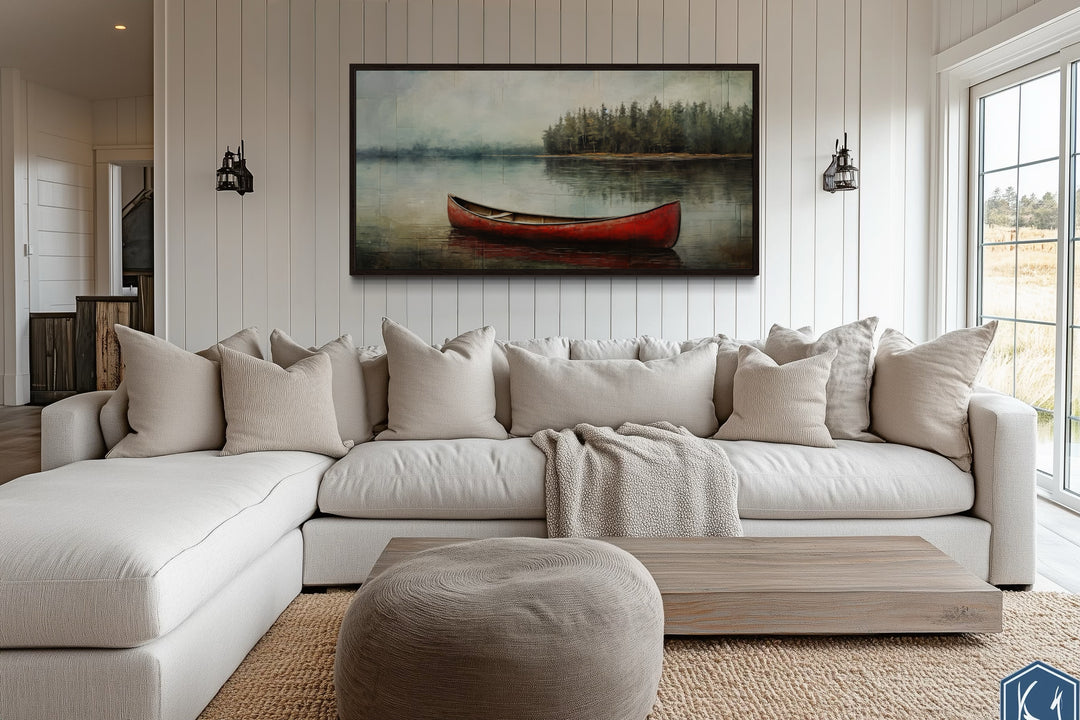 Rustic red canoe in a lake framed canvas wall art hanging above a white sectional sofa.