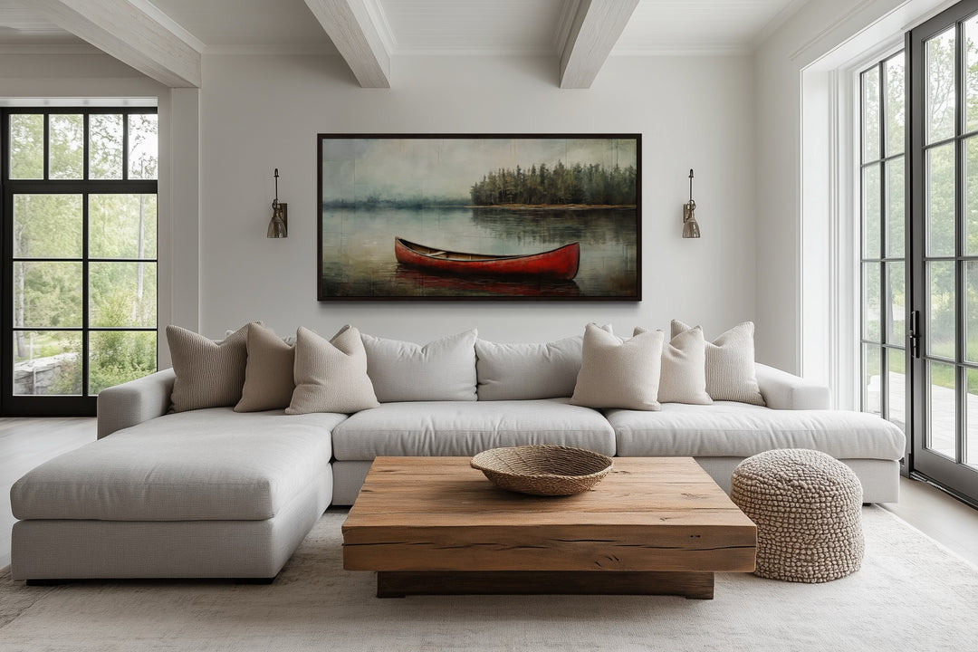 Rustic red canoe in a lake framed canvas wall art above a neutral sofa in a modern living room.