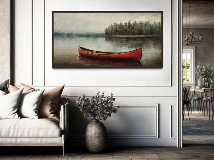 Rustic red canoe in a calm lake framed canvas wall art hanging above a sofa in a modern room.