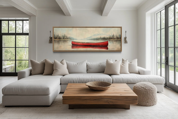 Rustic red canoe on a calm lake painted on a long wood-framed canvas above a modern sectional sofa.