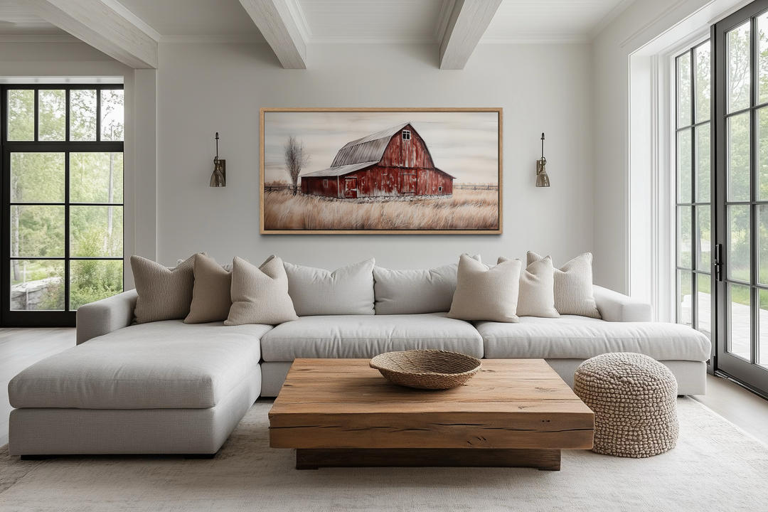 A rustic red barn painting on wood canvas hangs above a neutral sofa in a farmhouse living room.