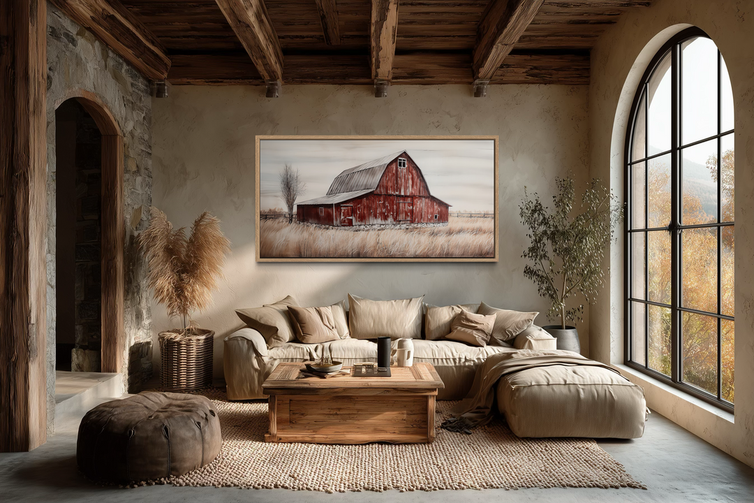 A rustic red barn painting on canvas hangs above a neutral sofa in a farmhouse-style living room.