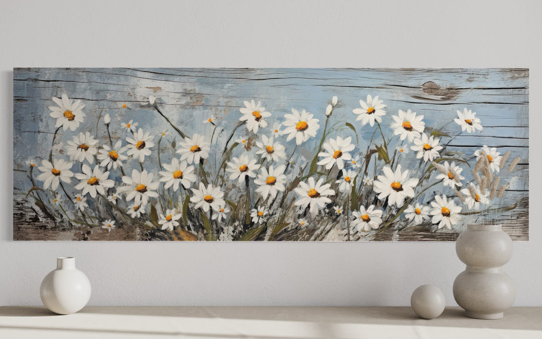 Rustic horizontal wall art of white daisies painted on a weathered blue wood background.
