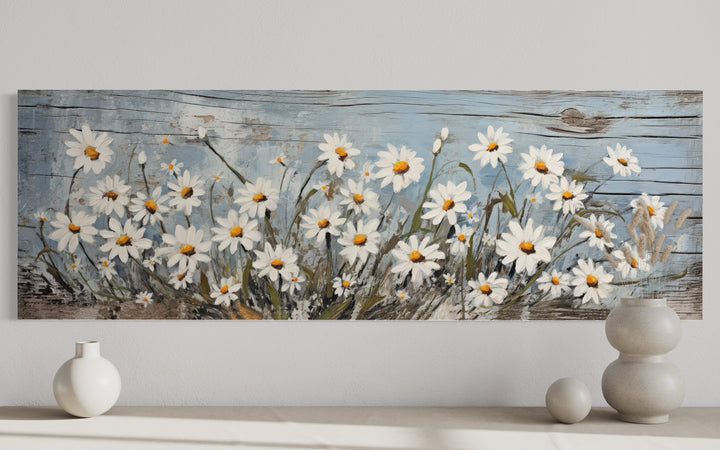 Rustic horizontal wall art of white daisies painted on a weathered blue wood background.