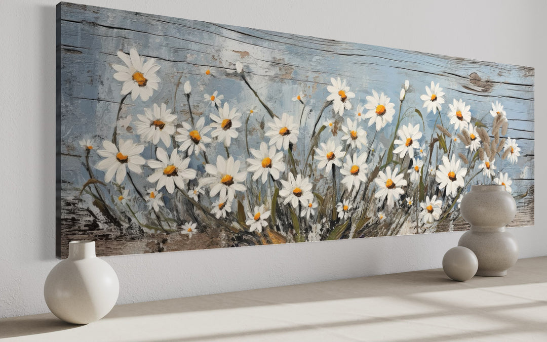 Rustic horizontal wall art of white daisies painted on a weathered blue wood background.