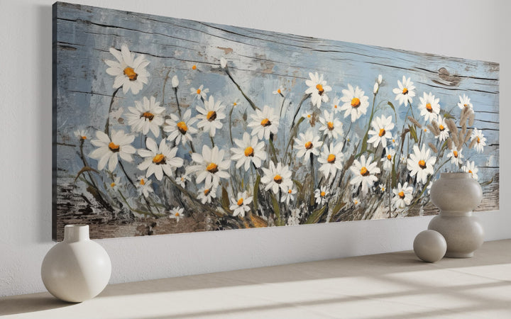 Rustic horizontal wall art of white daisies painted on a weathered blue wood background.