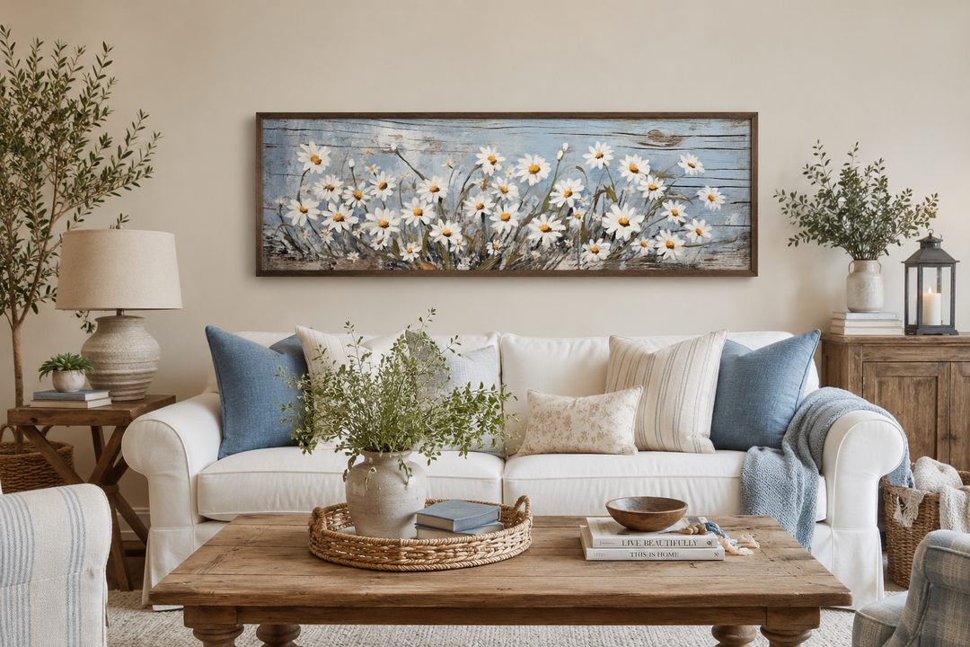 Rustic white daisies painted on blue wood long horizontal wall art framed above a white sofa.