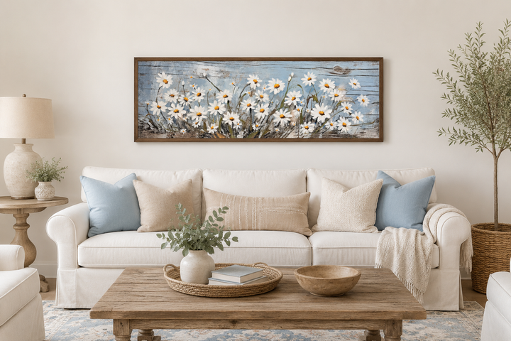 Rustic white daisies painted on blue wood long horizontal wall art framed above a white sofa.