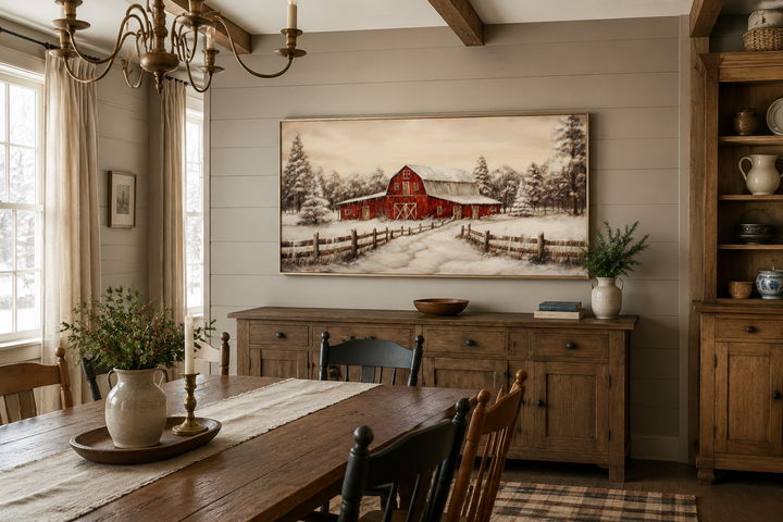Framed canvas wall art of a red barn in a snowy winter landscape above a wooden sideboard.