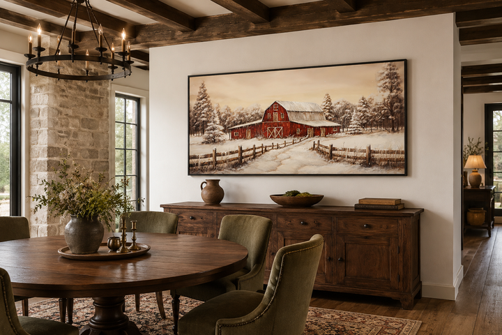 Framed canvas wall art of a red barn in a snowy winter landscape above a wooden sideboard.