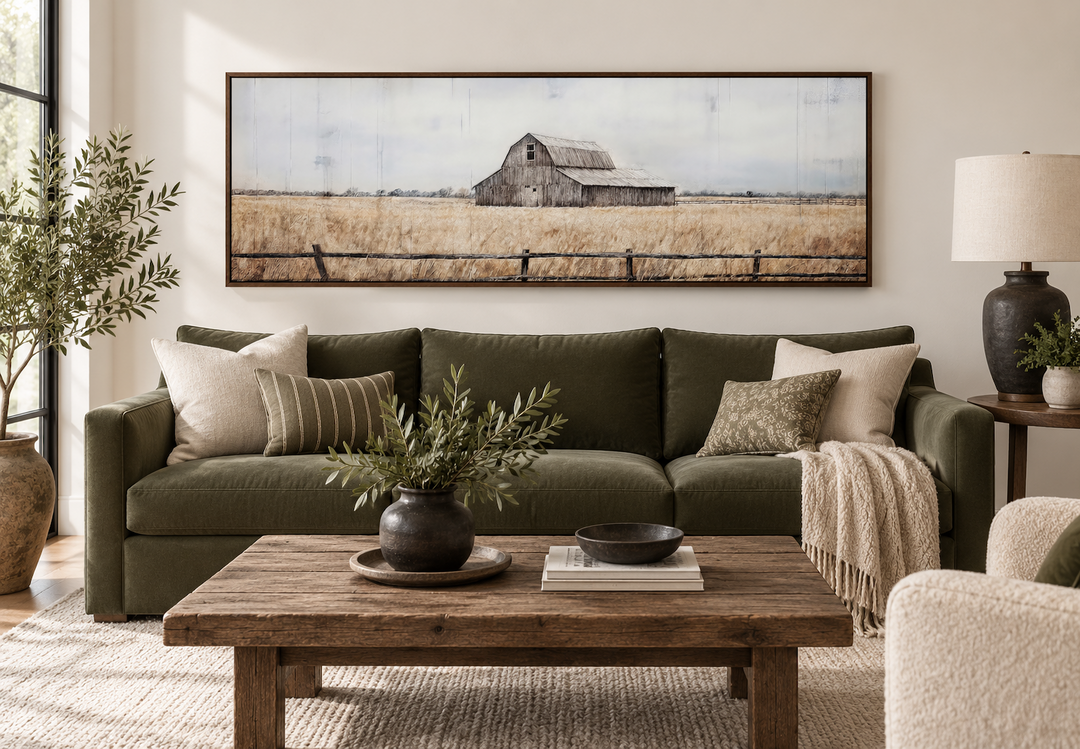 Rustic old barn painting on long narrow framed canvas wall art above a green sofa in a living room.
