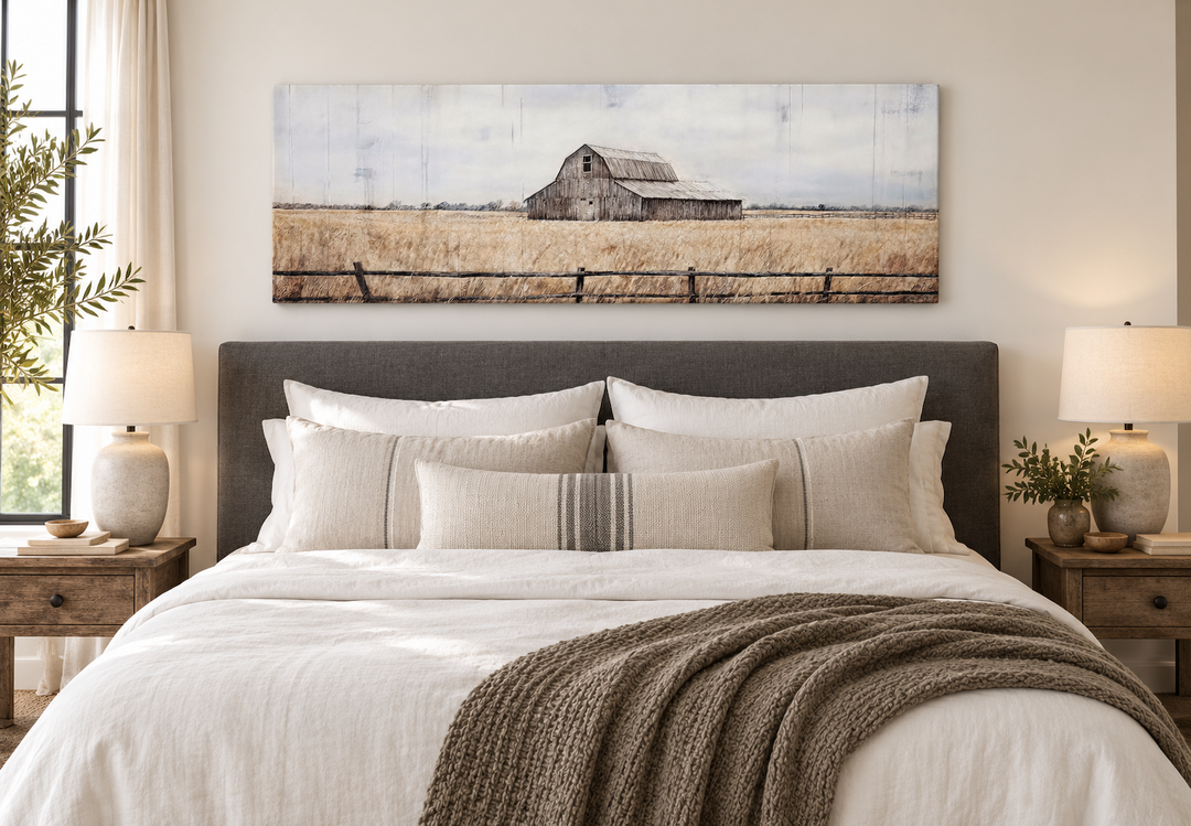 Rustic old barn painting on long narrow canvas wall art above a bed in a farmhouse bedroom.