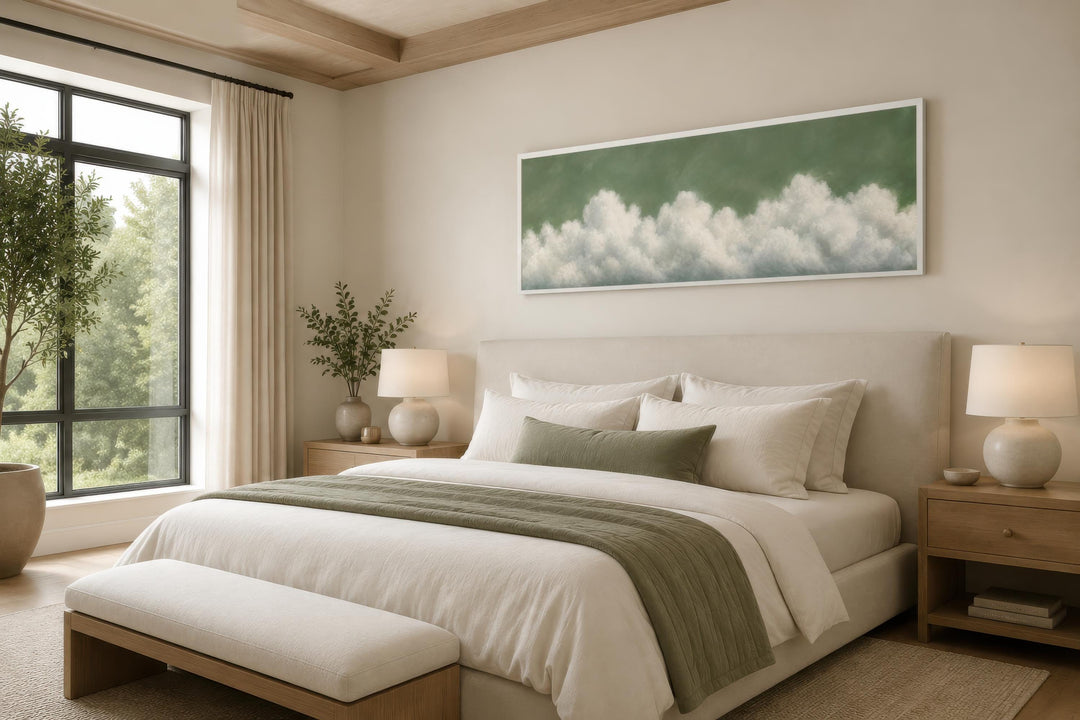 Sage green long narrow canvas wall art with soft white clouds hanging above a bed in a bedroom.