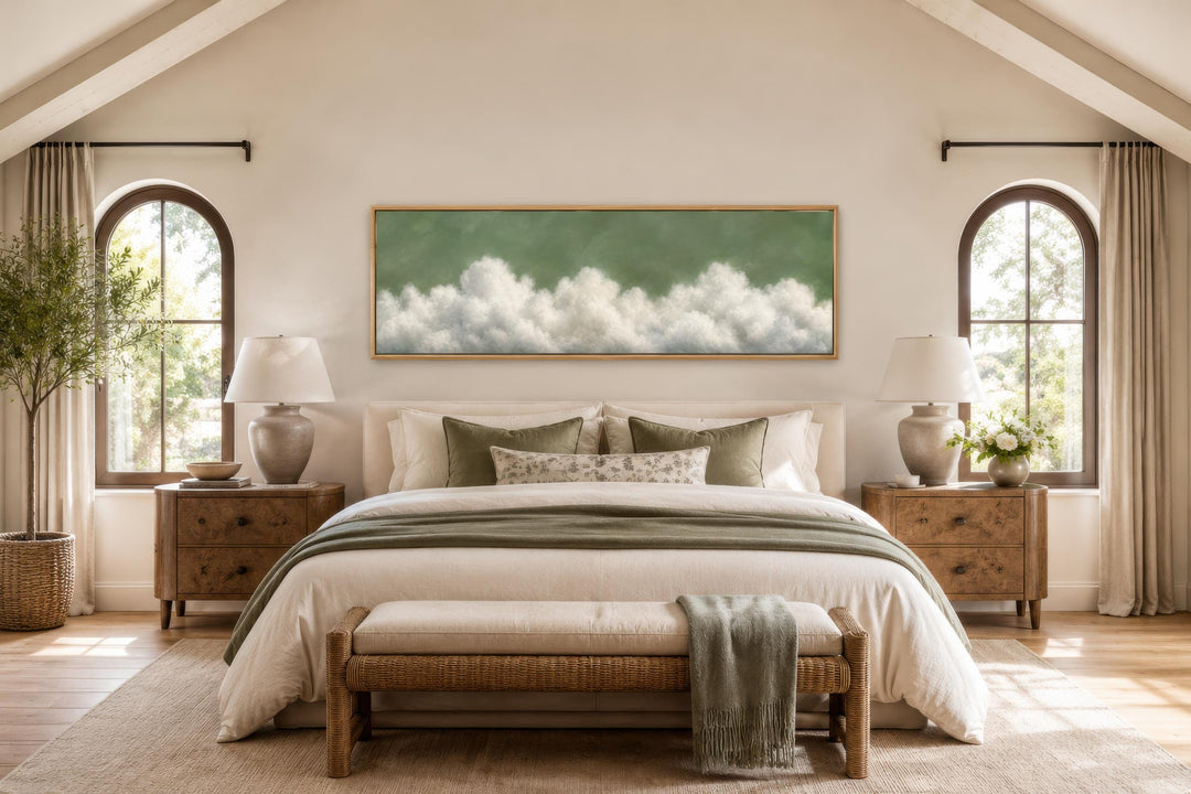 Long narrow sage green canvas wall art with soft white clouds hanging above a neutral-toned bed.